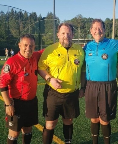 Three referees in red, yellow, and blue shirts on a soccer field