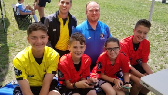 Young referees and two adults gathered beside a soccer field