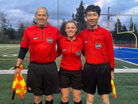 Three referees standing together in red shirts on a soccer field